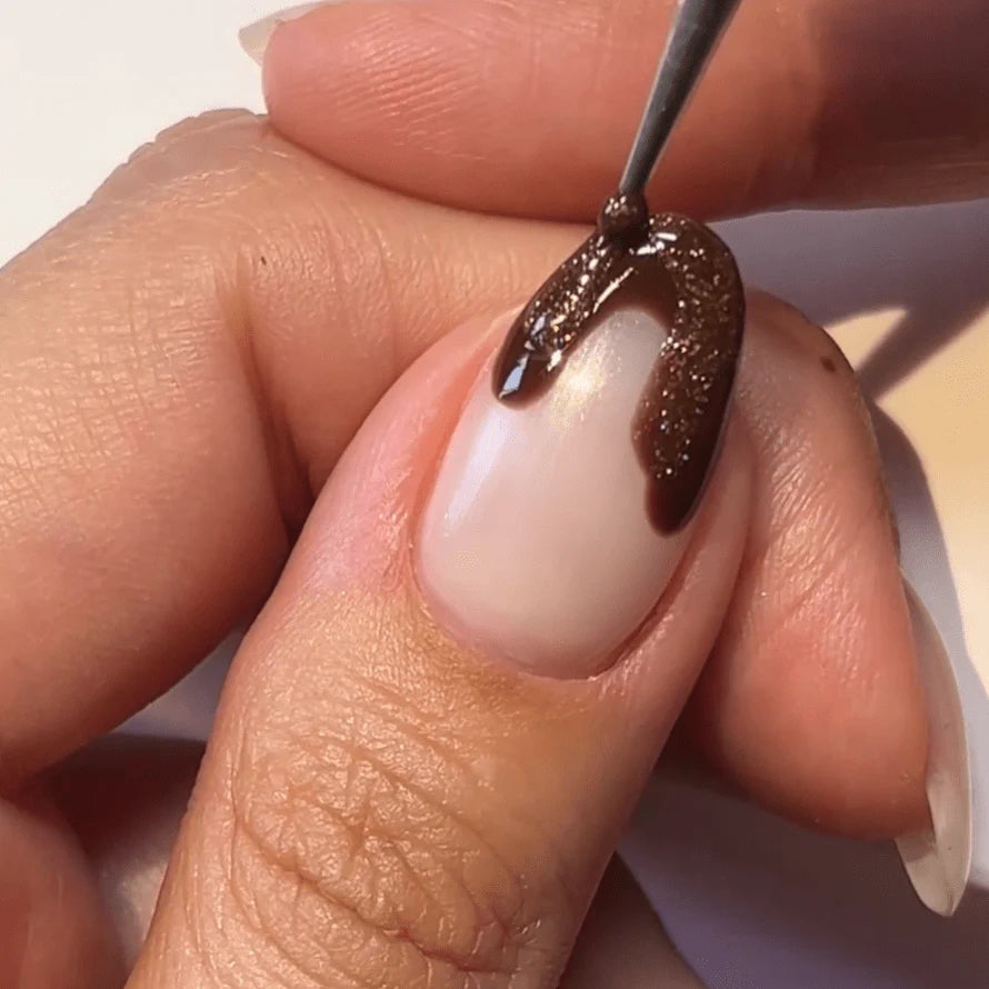 A hand holding another hand while applying brown nail polish to a nail.