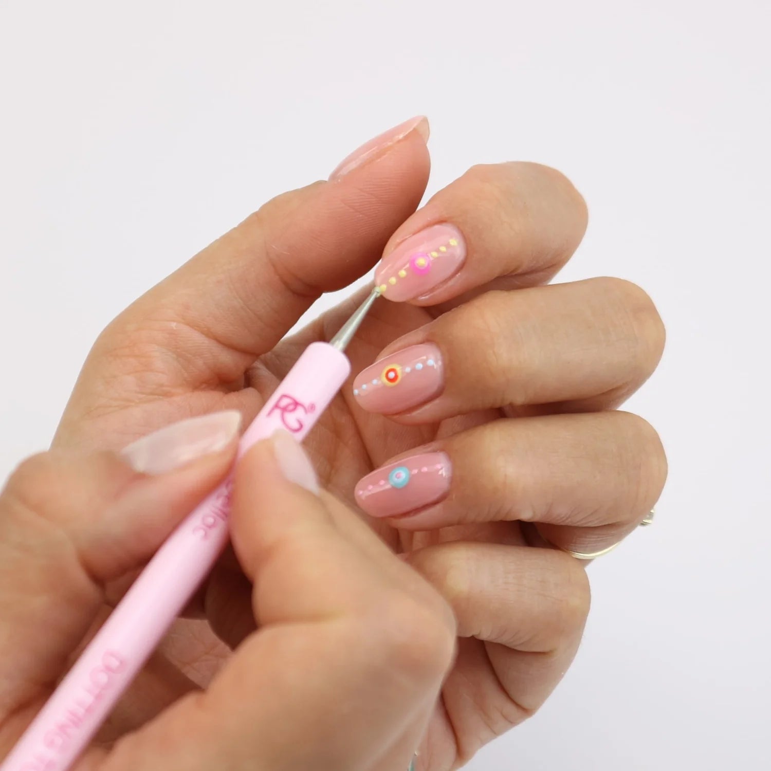 Two hands where the nails of one hand are decorated with a pink dotting tool, where each nail has a colorful dot pattern on a light pink background.
