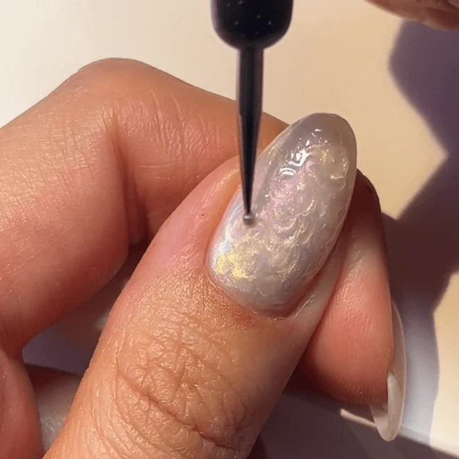 Close-up of a hand with long, shiny nails being decorated with a thin brush.