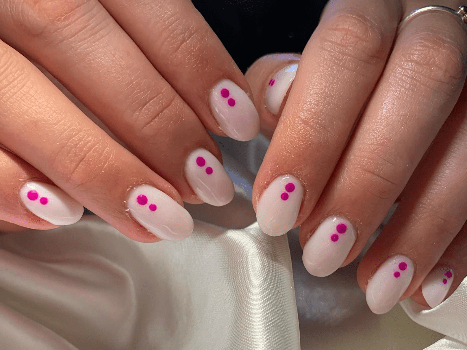 Close-up of hands with shiny white nail polish and pink dots on each nail.