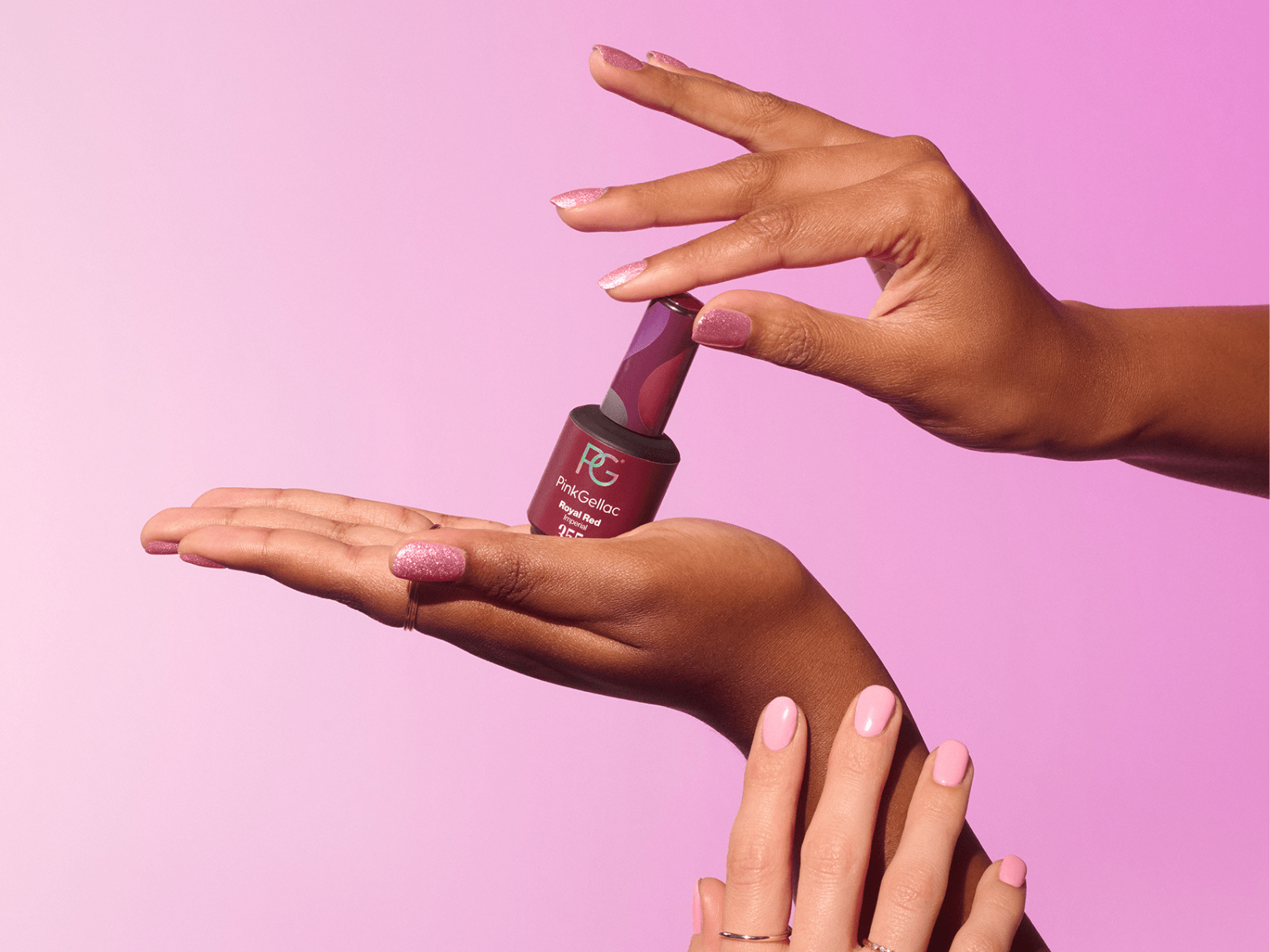 Hands with pink nail polish showing a bottle of Pink Gellac nail polish against a pink background.