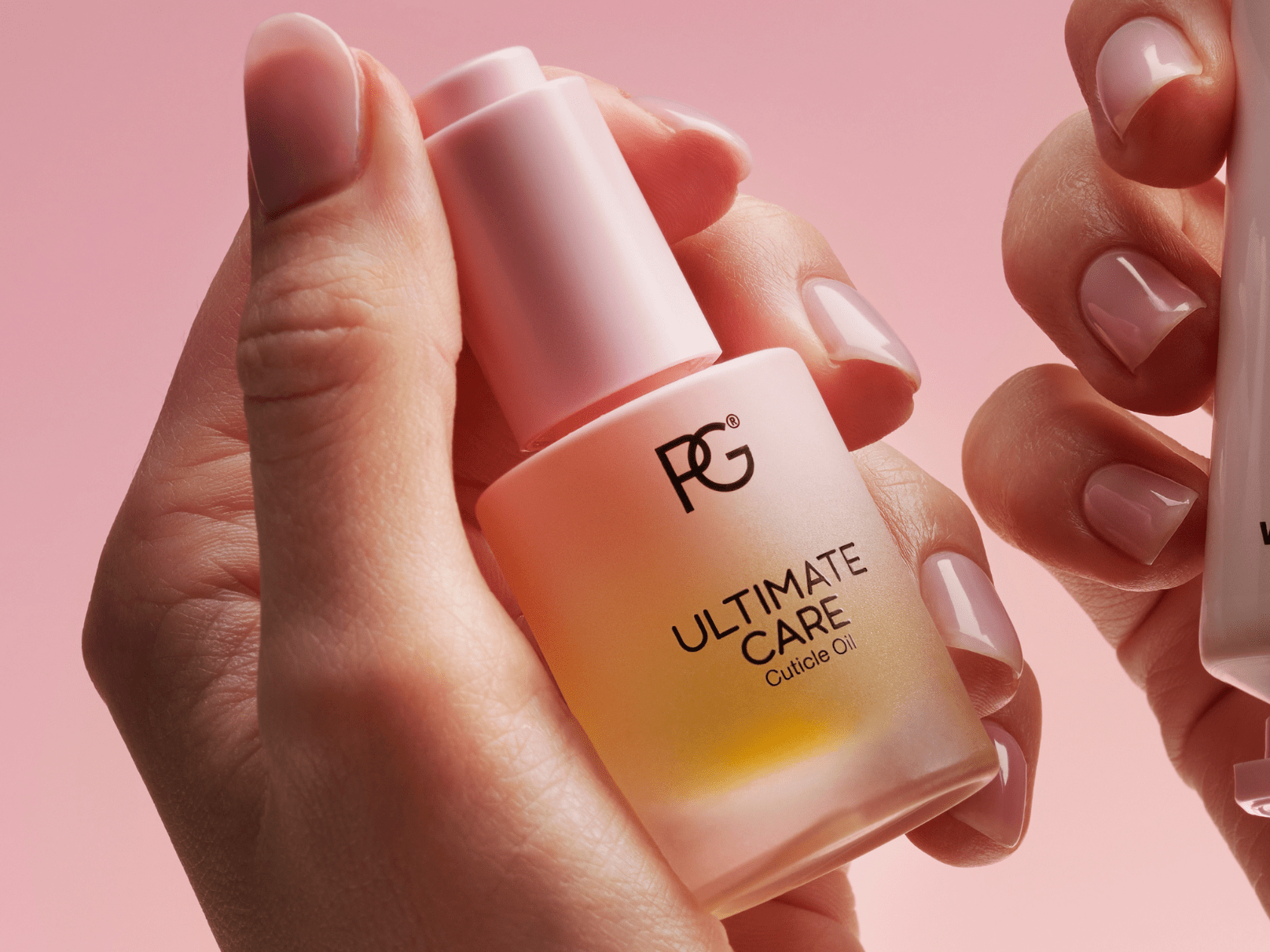 Hands holding a bottle of cuticle oil with pink background.