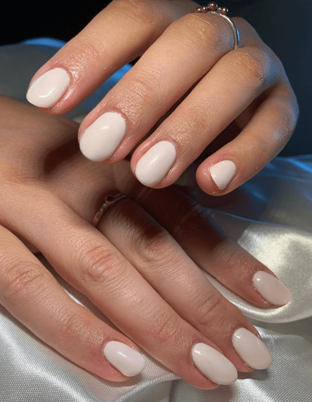 Polished hands with shiny light pink nail polish on a satin background.