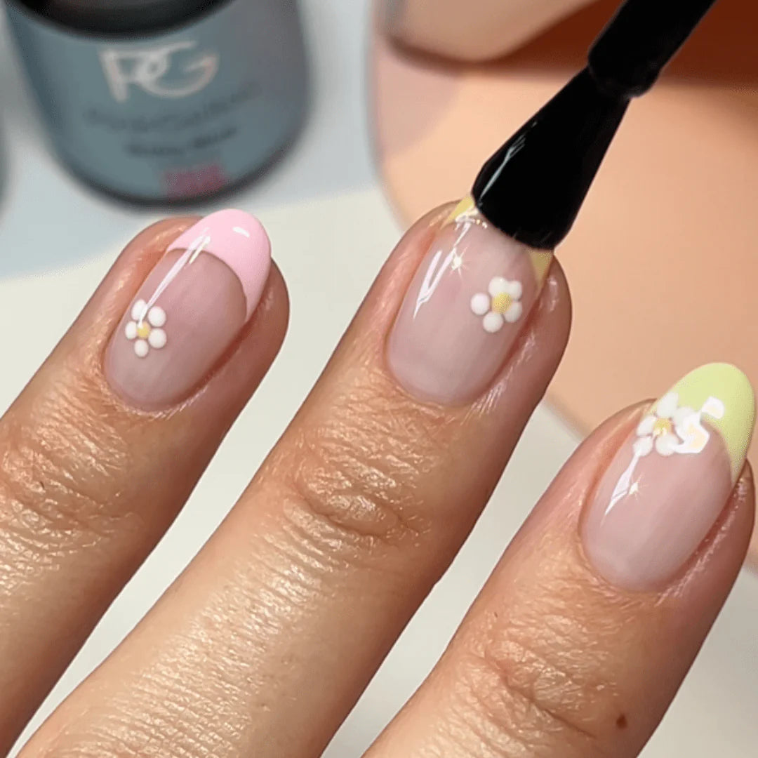Close-up of a hand with nails painted in pastel colors and decorated with small flowers, with a brush touching one of the nails.